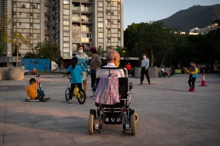 man in electric wheelchair watching active kids play